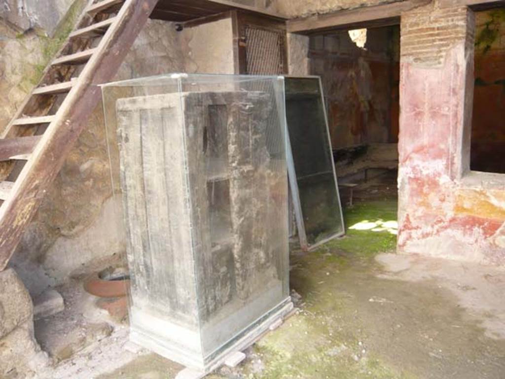 V 17, Herculaneum, Herculaneum. May 2009. Looking towards east side with remains of a cupboard/wardrobe. Photo courtesy of Buzz Ferebee. 
In the space under the steps can be seen a dolium buried into the ground, and nearby was a terracotta oven. On the left through the doorway to the rear room, the remains of a carbonized wooden bed can be seen.